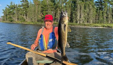 Stu Osthoff in a canoe holding up a walleye in the Boundary Waters.